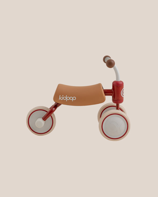Red and tan BEE Baby Balance Bike for toddlers with tan seat featuring 'kidpop' logo and cream wheels, showcasing product.