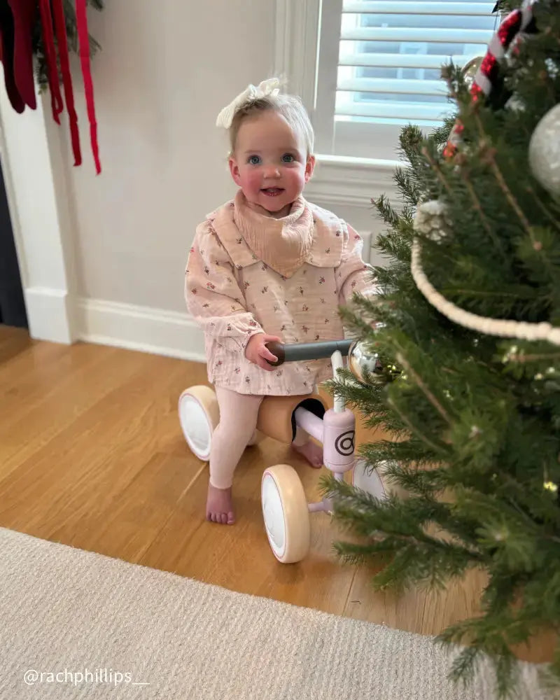 Baby girl with white bow and pink floral outfit on a BIG BEE baby balance bike.