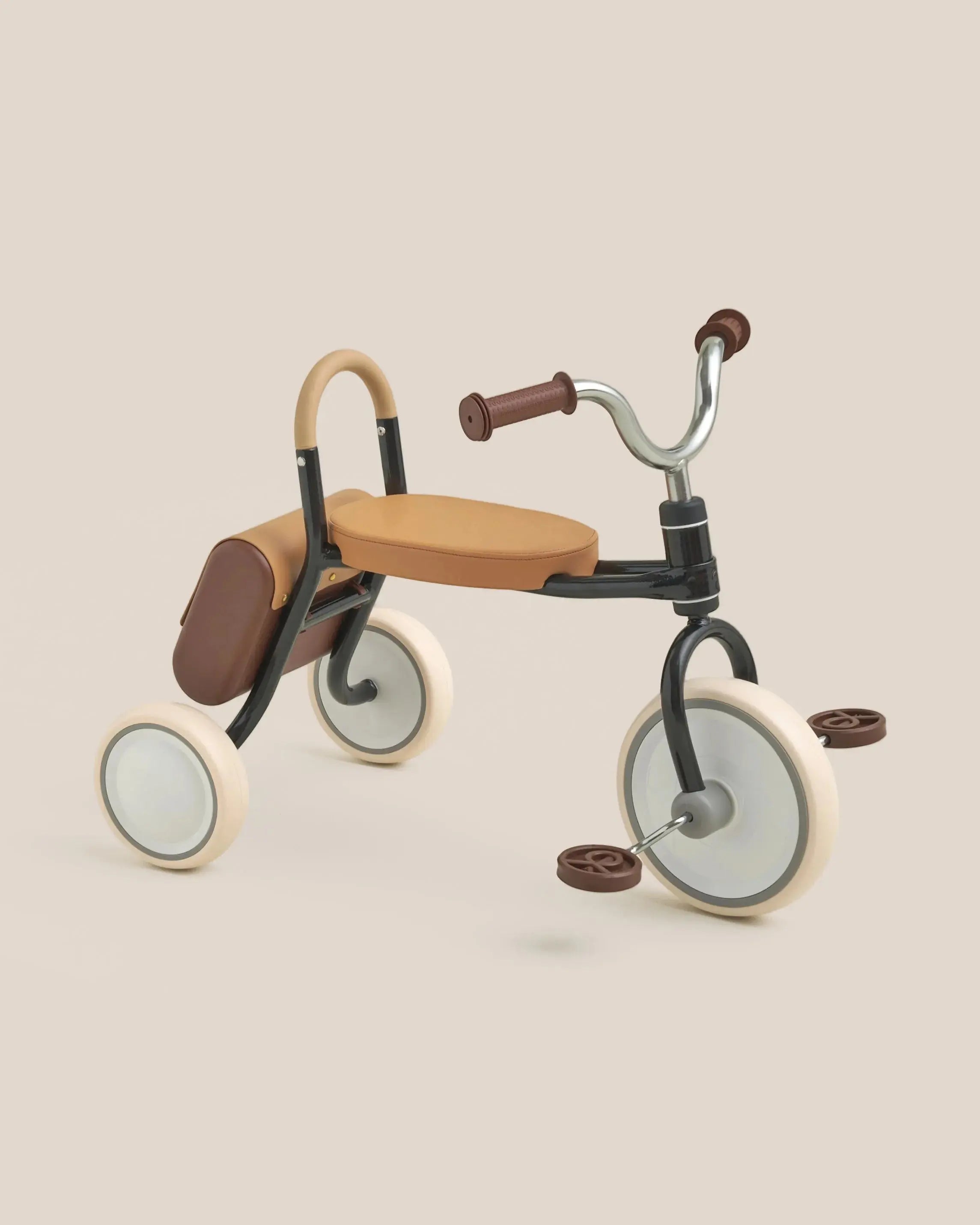 MATE Kids' tricycle with black frame, tan seat, brown handlebars, and saddle bag. Cream wheels with tan accents.