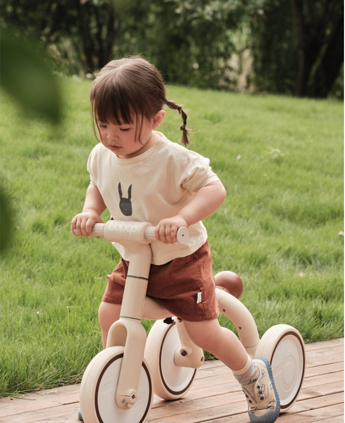  Toddler riding a cream-colored Kidpop balance bike on a grassy lawn.