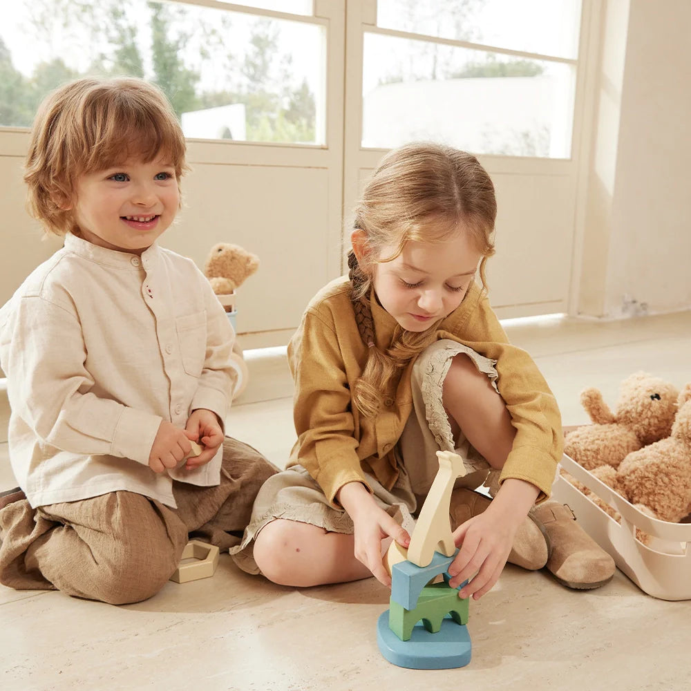 A young boy and girl sit on the floor playing with wooden stacking toys.