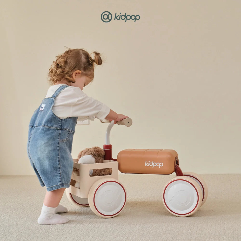 Toddlers playing with a red wagon and a Kidpop balance bike indoors.