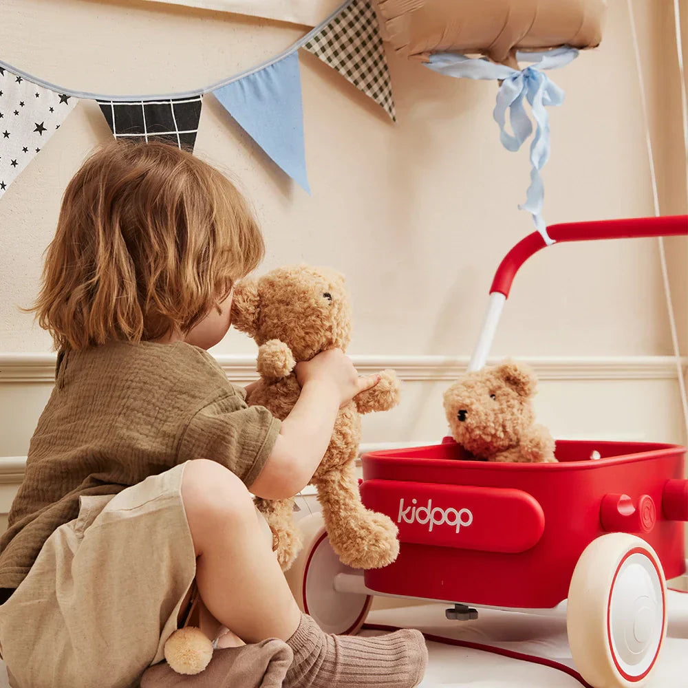 Toddler playing with a red Kidpop wagon and teddy bears in a festive playroom.