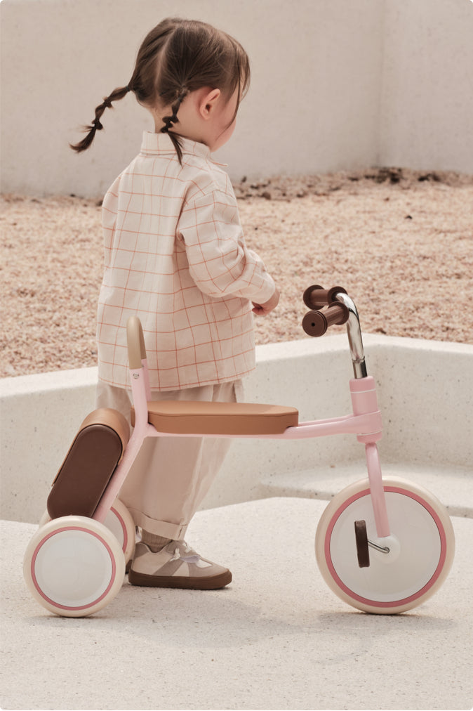 Little girl with pigtails standing next to a pink Kidpop vintage tricycle.