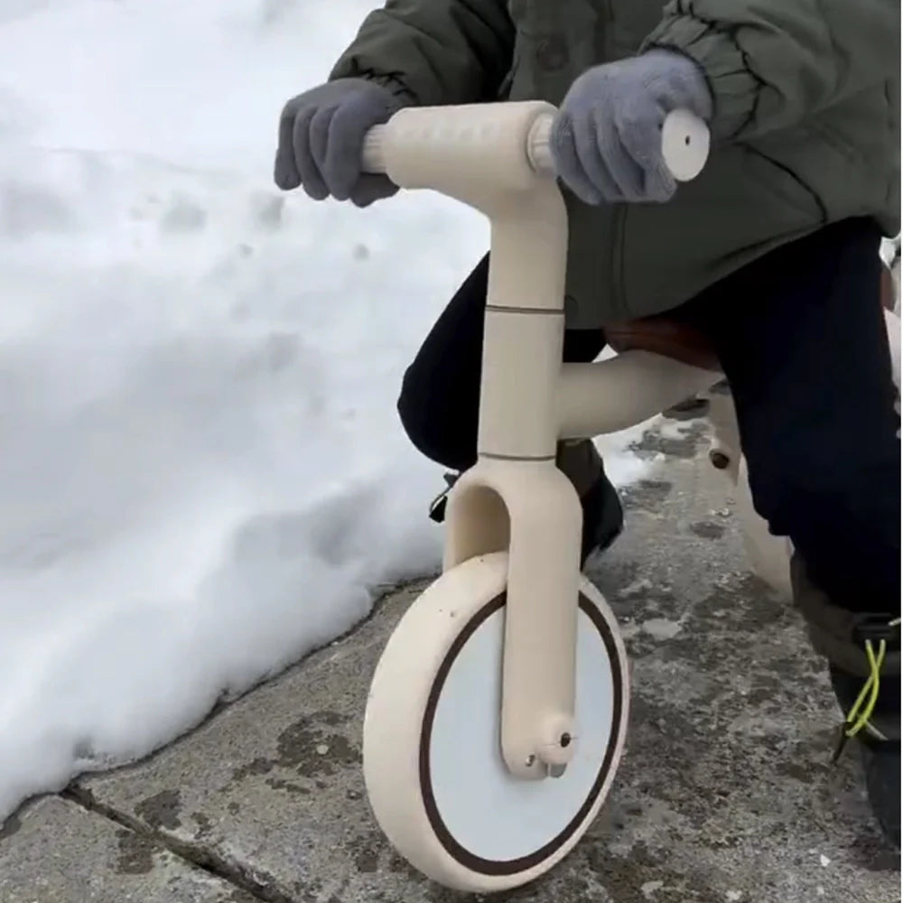 Kidpop cream balance bike being ridden by a child in gloves on a snowy path.