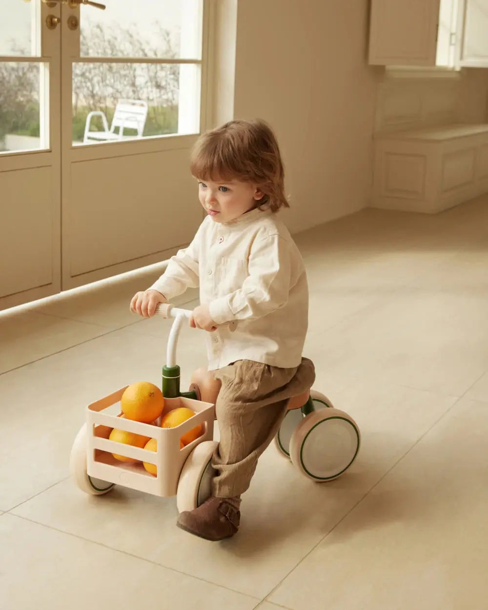 Child riding a beige TOAST baby balance bike with a basket of oranges