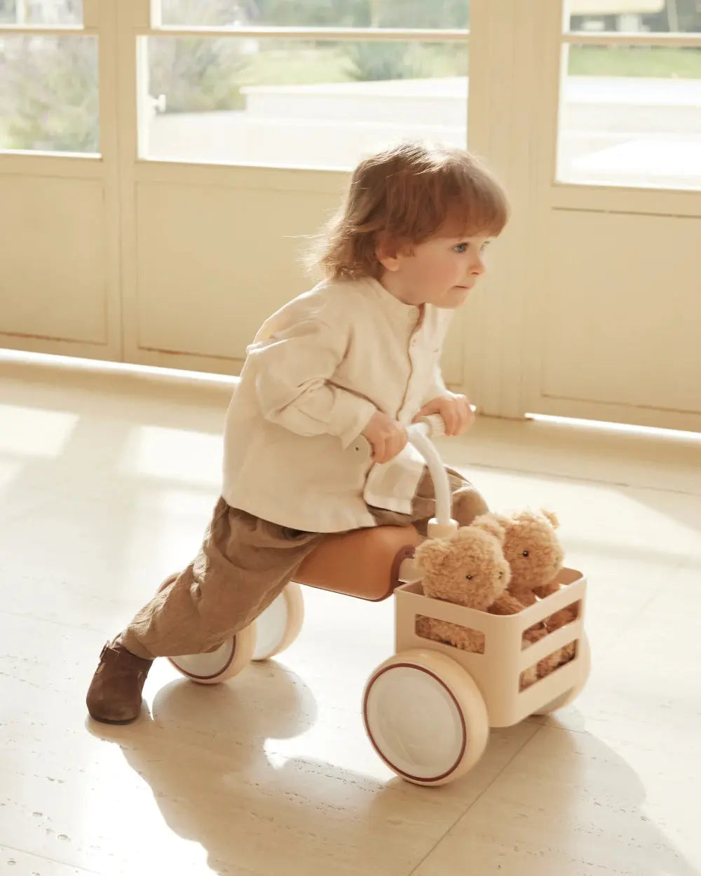 Beige TOAST baby balance bike with a child riding it and two teddy bears in the front basket.