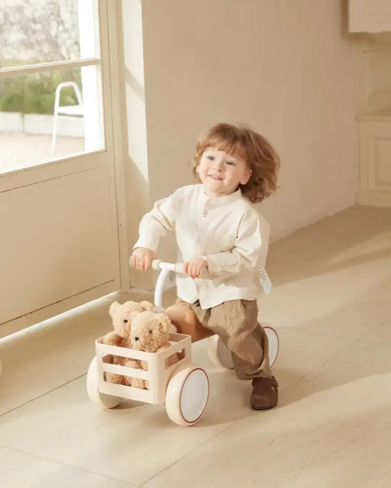 Child riding beige Kidpop TOAST Baby Balance Bike with teddy bears in basket.